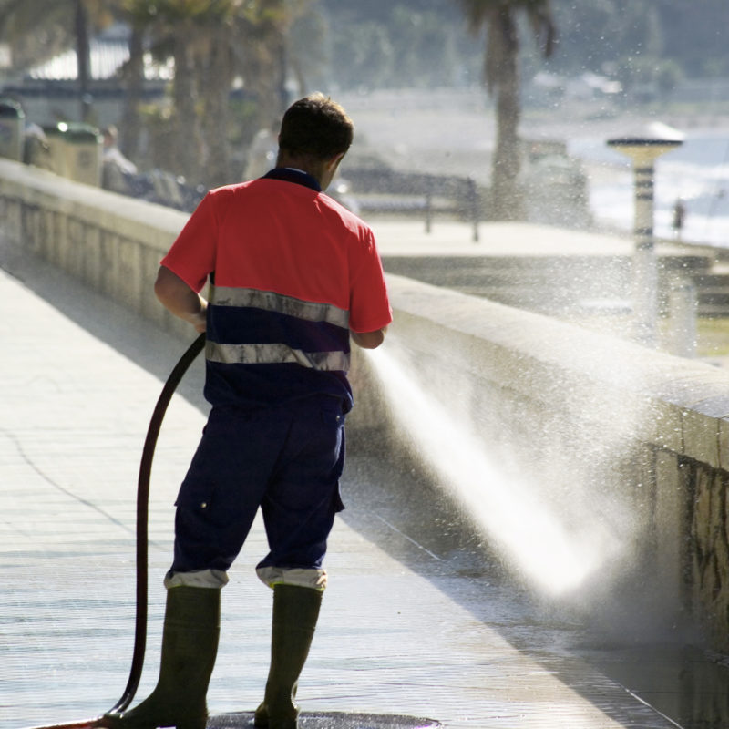 Workman spray cleaning an outdoor area with a power washer