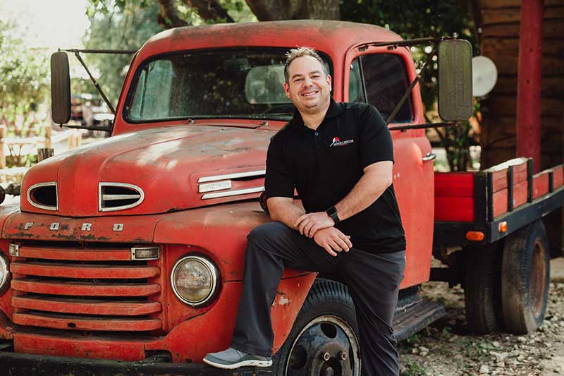 A man in a black shirt poses with a red truck, representing PDS's innovation in construction